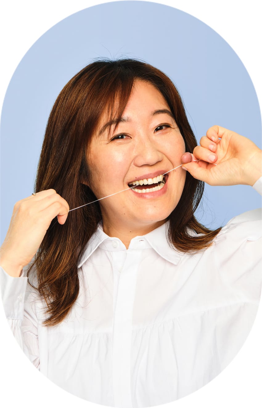 A person is smiling wide, while running a piece of dental floss through their front teeth.