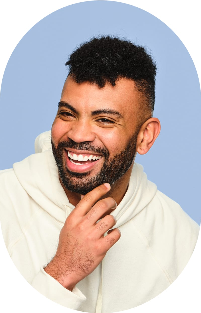 A man with curly hair is looking to the left. He is smiling, and his hand is on his chin.