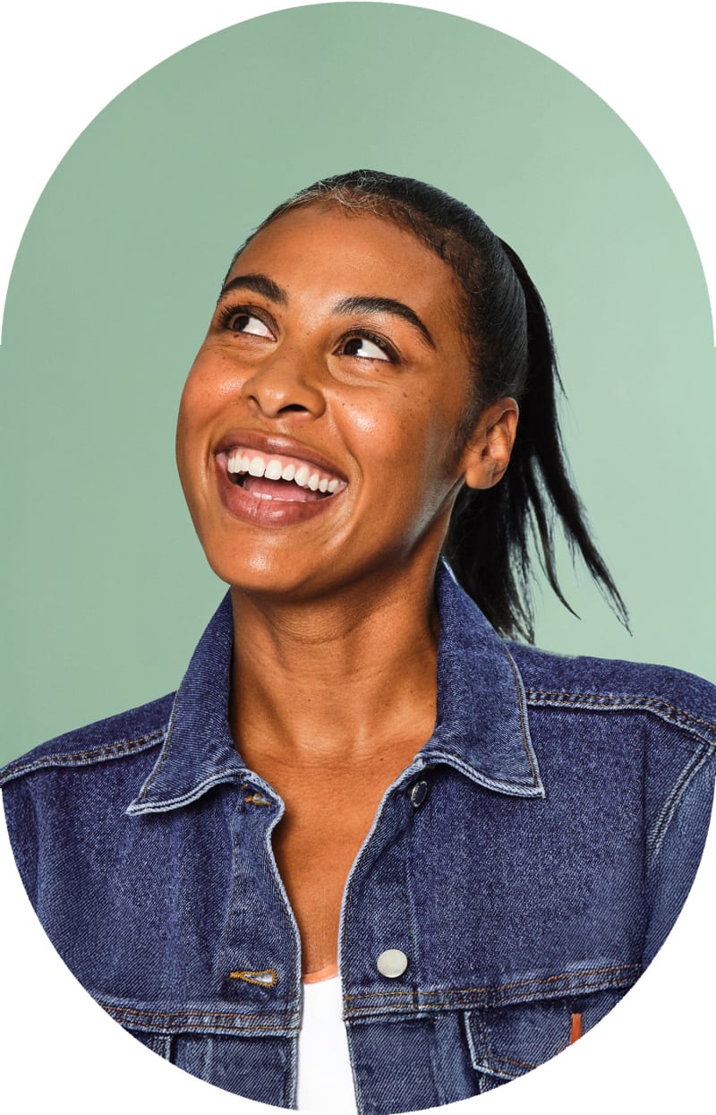 A woman is smiling and looking to the left. She is wearing a denim jacket.