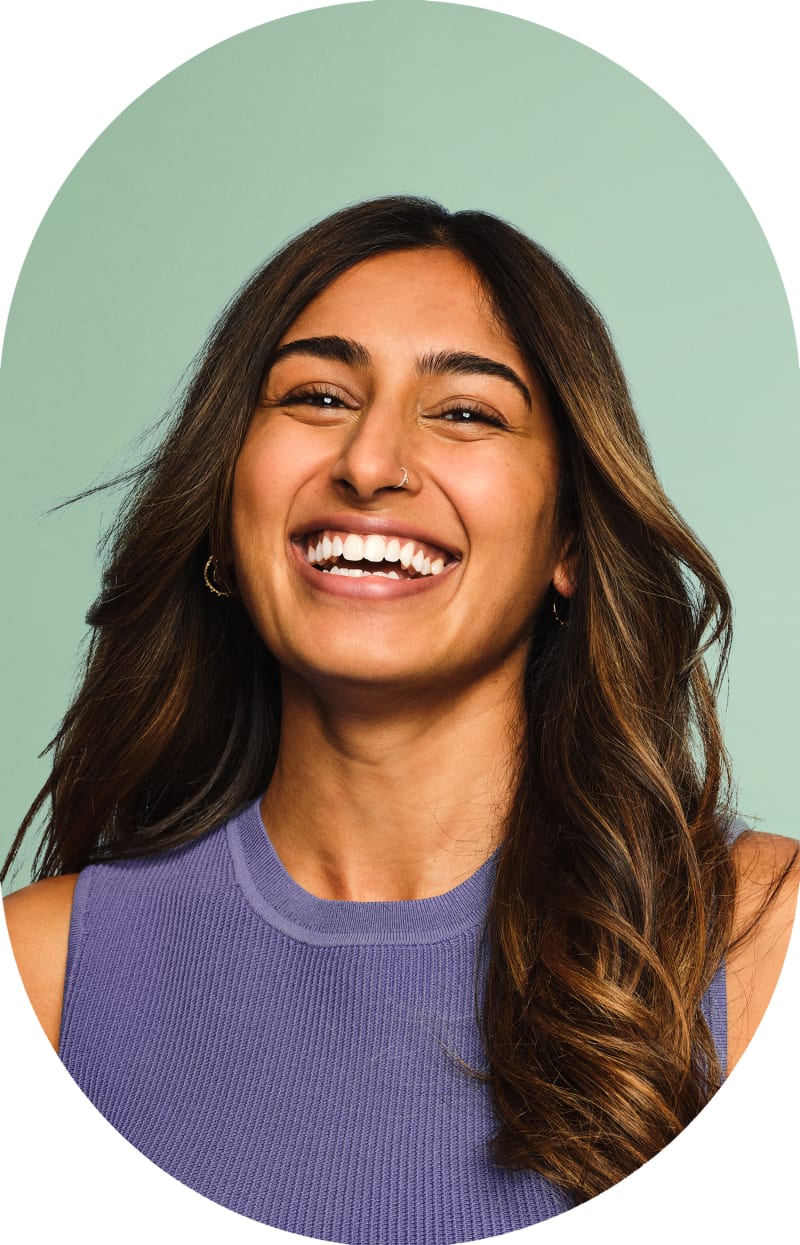 A woman with long hair and a nose piercing is smiling and looking up.