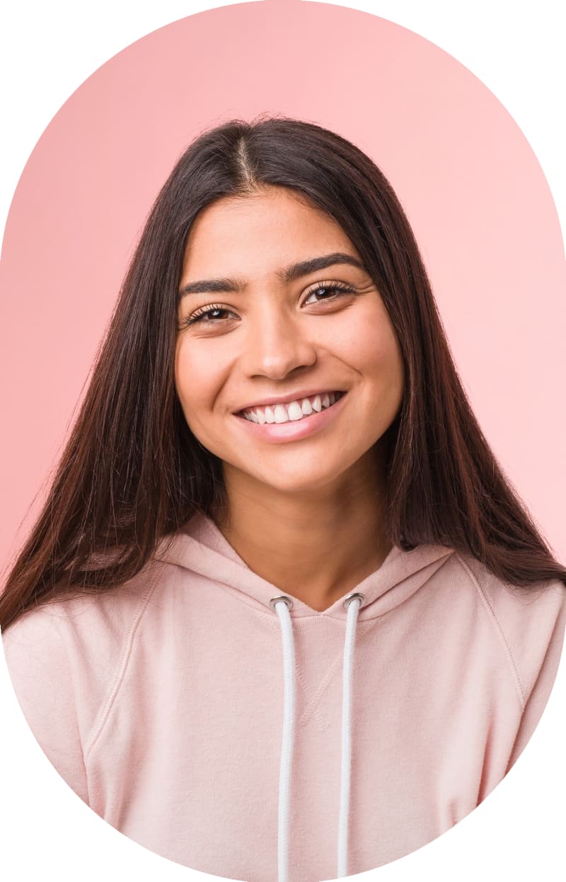A teenage girl with long straight brown hair is smiling. She is wearing a pink hoodie.