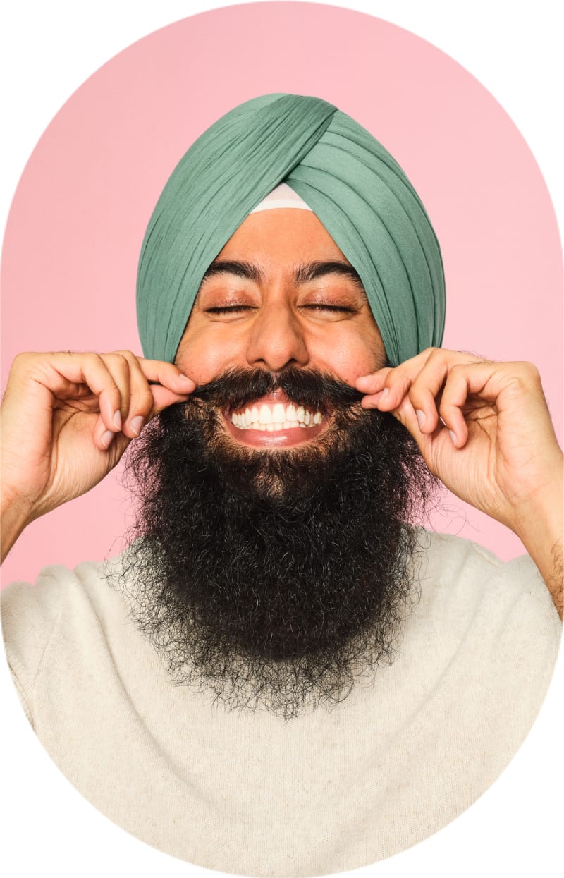 A man with lots of facial hair is smiling widely and twirling his mustache.