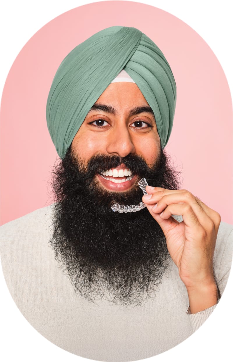 A man with a long beard is smiling and holding clear aligners up to his mouth.