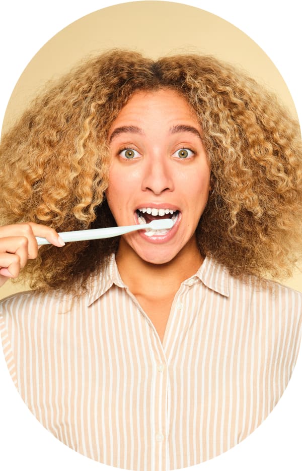 A woman is brushing her teeth and making a surprised face.