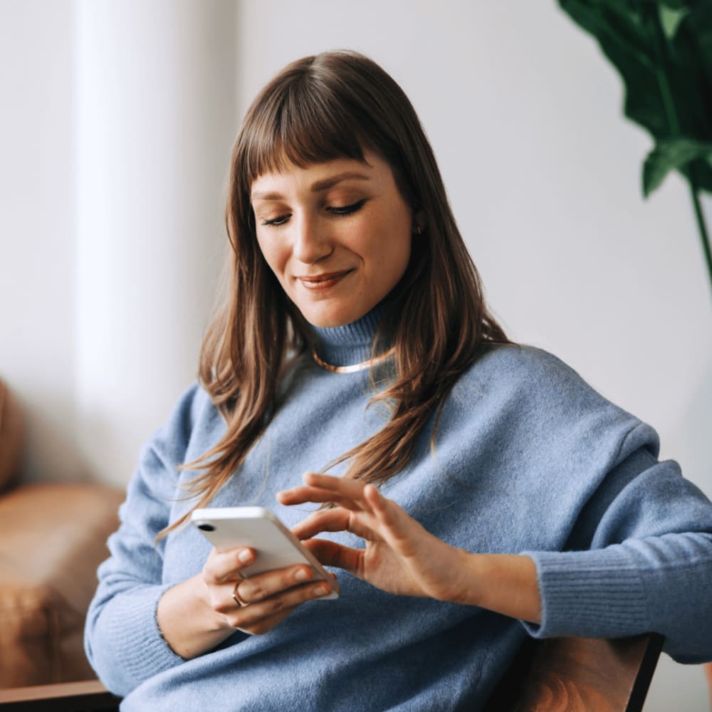 A woman is sitting in a comfy chair scrolling on her phone.