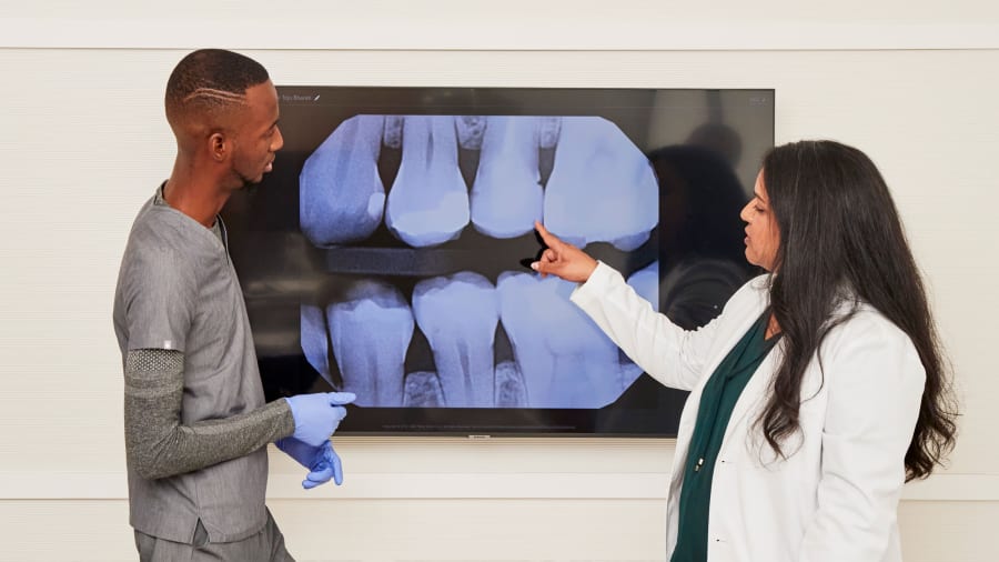 Two team members looking at a large digital X-ray of teeth. One team member is pointing at something on the X-ray.