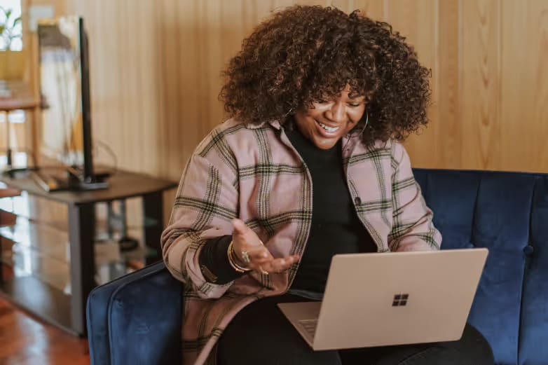 Woman sitting on a sofa, chatting with someone on her laptop screen.