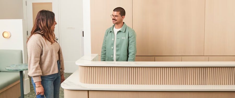 Team member behind reception desk chatting with client on other side of the desk.