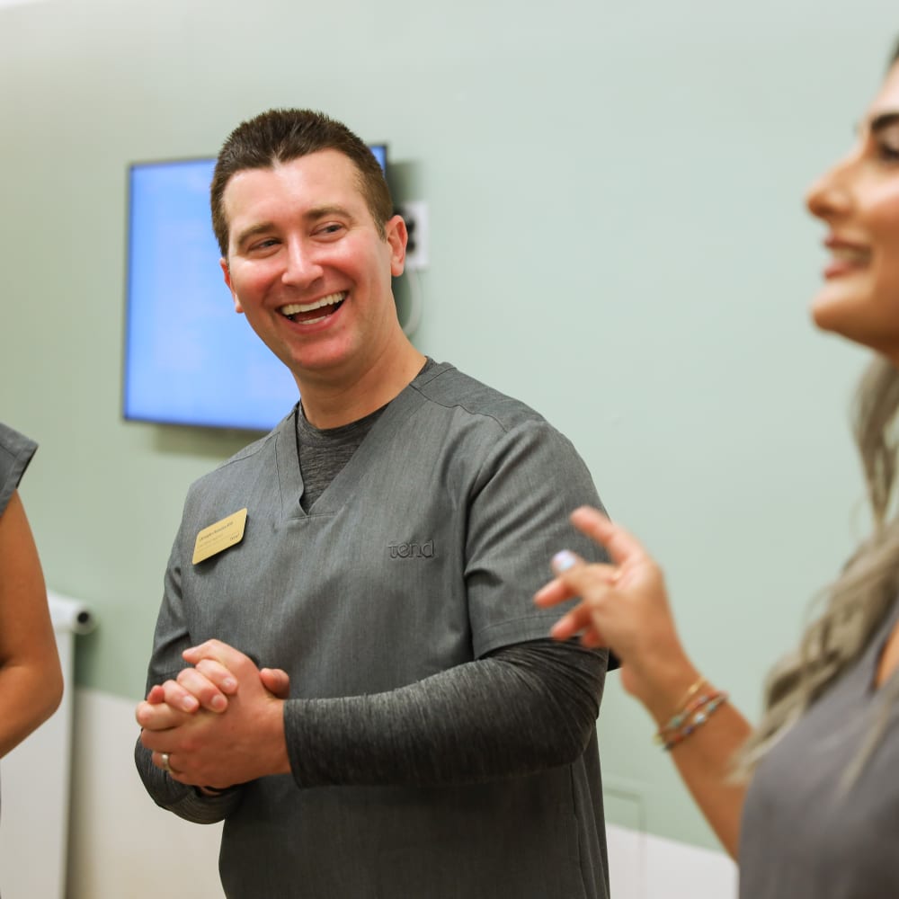 A male Tend Dental team member is smiling with his hands clasped.