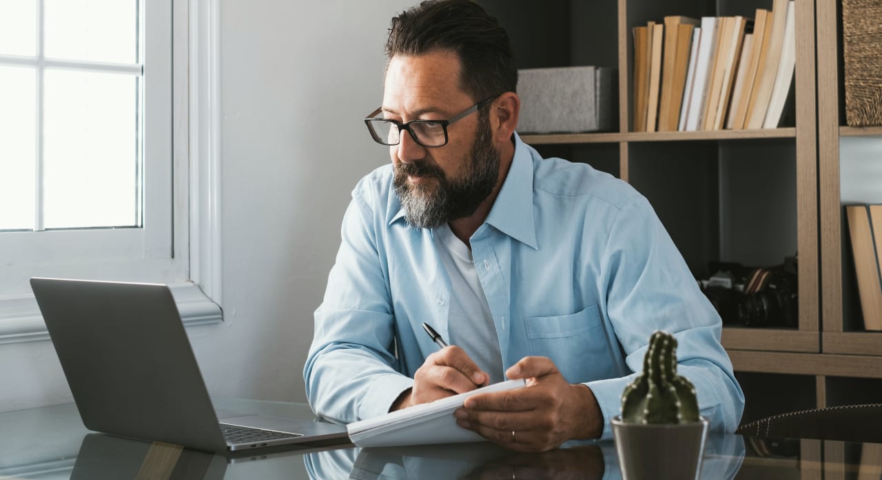 A man is looking at a laptop and taking notes.