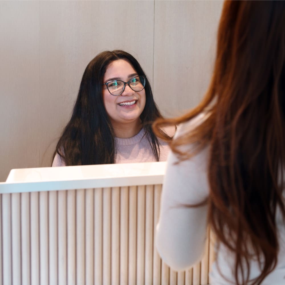 A Tend employee is sitting behind a reception desk talking to a patient.