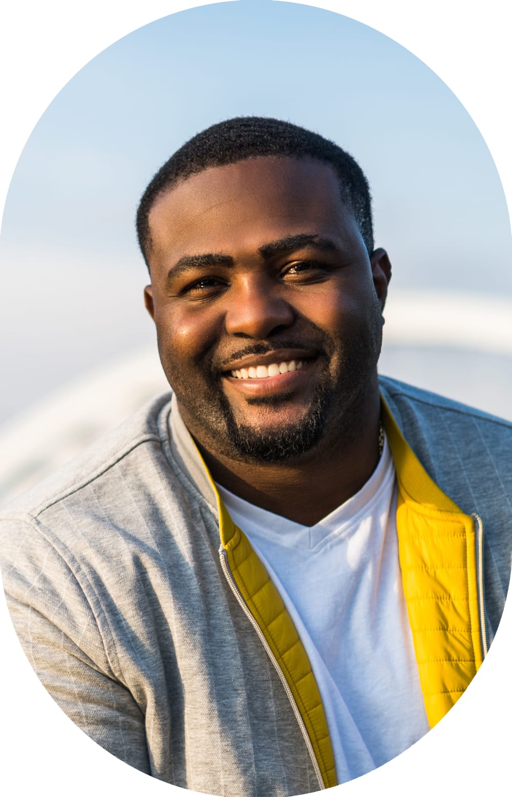 A bunsiness man with a bag strap over his shoulder stands outside smiling.