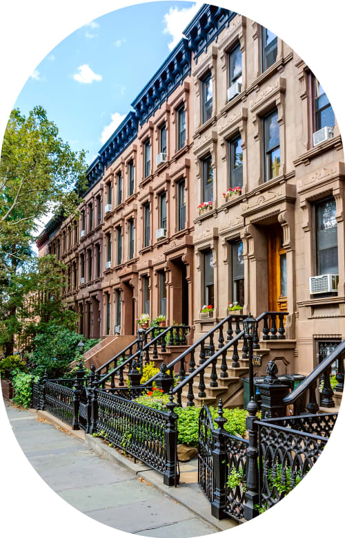 View of the front of a block of low rise homes with iron fenced front yards and some trees,