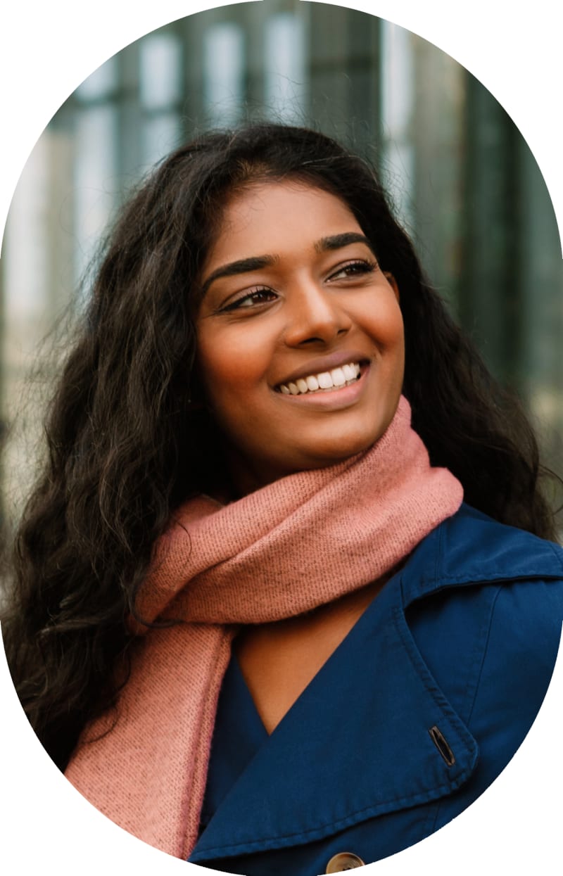 A woman in a blue jacket and pink scarf is looking to the right and smiling.