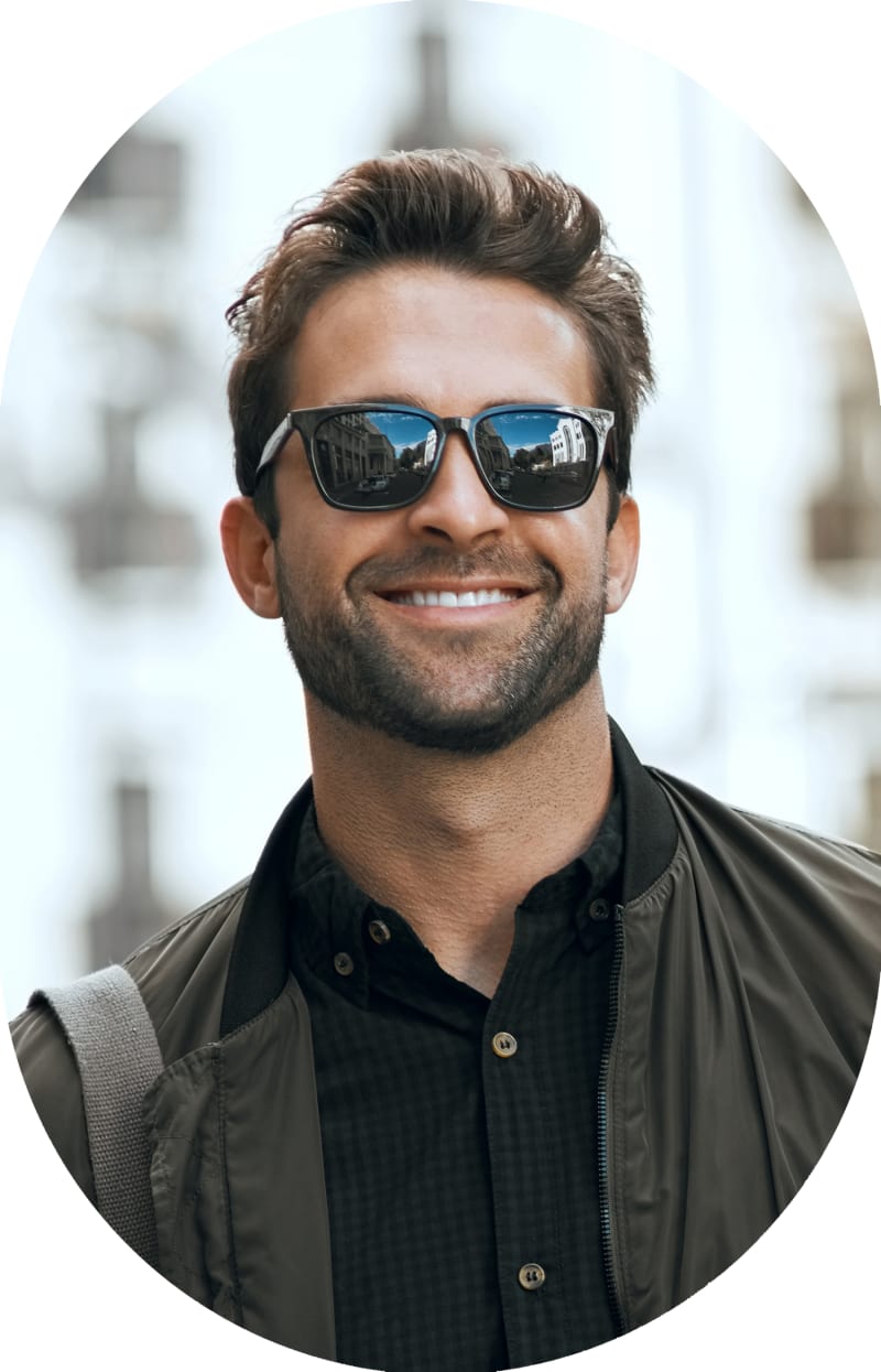 A man in a dark shirt and sunglasses is smiling.