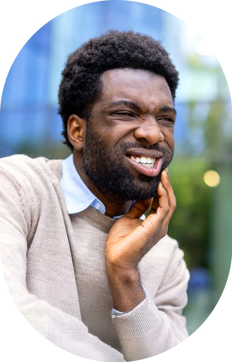 A man sits outside holding his hand to face indicating tooth discomfort.