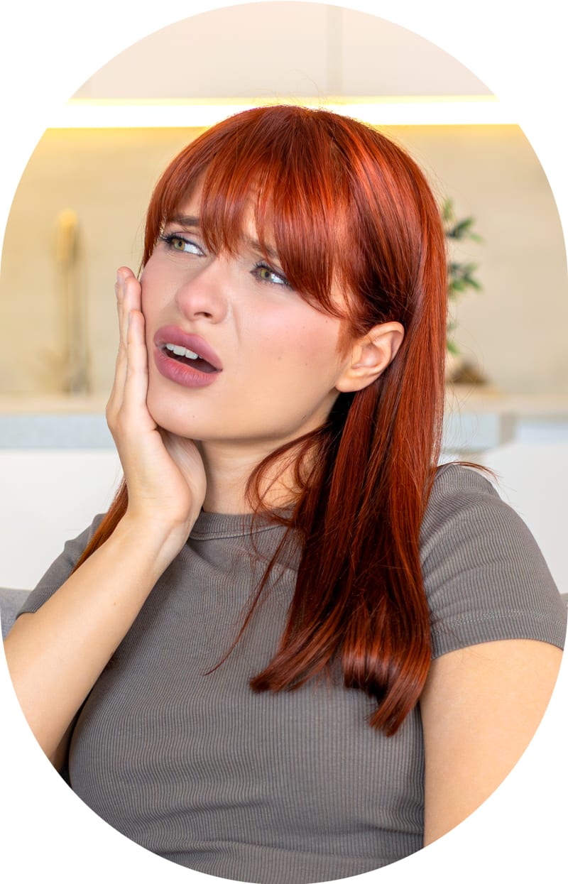 A woman stands inside holding a hand to her face indicating tooth discomfort.