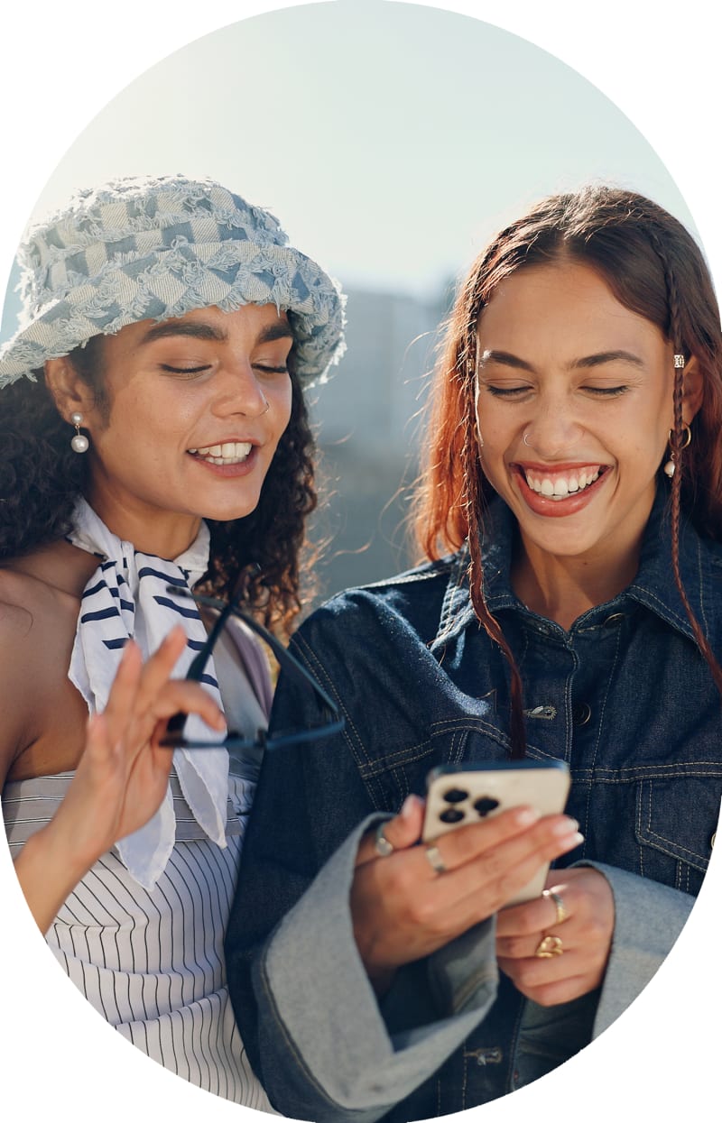 Two women are smiling and laughing while looking at a smartphone.