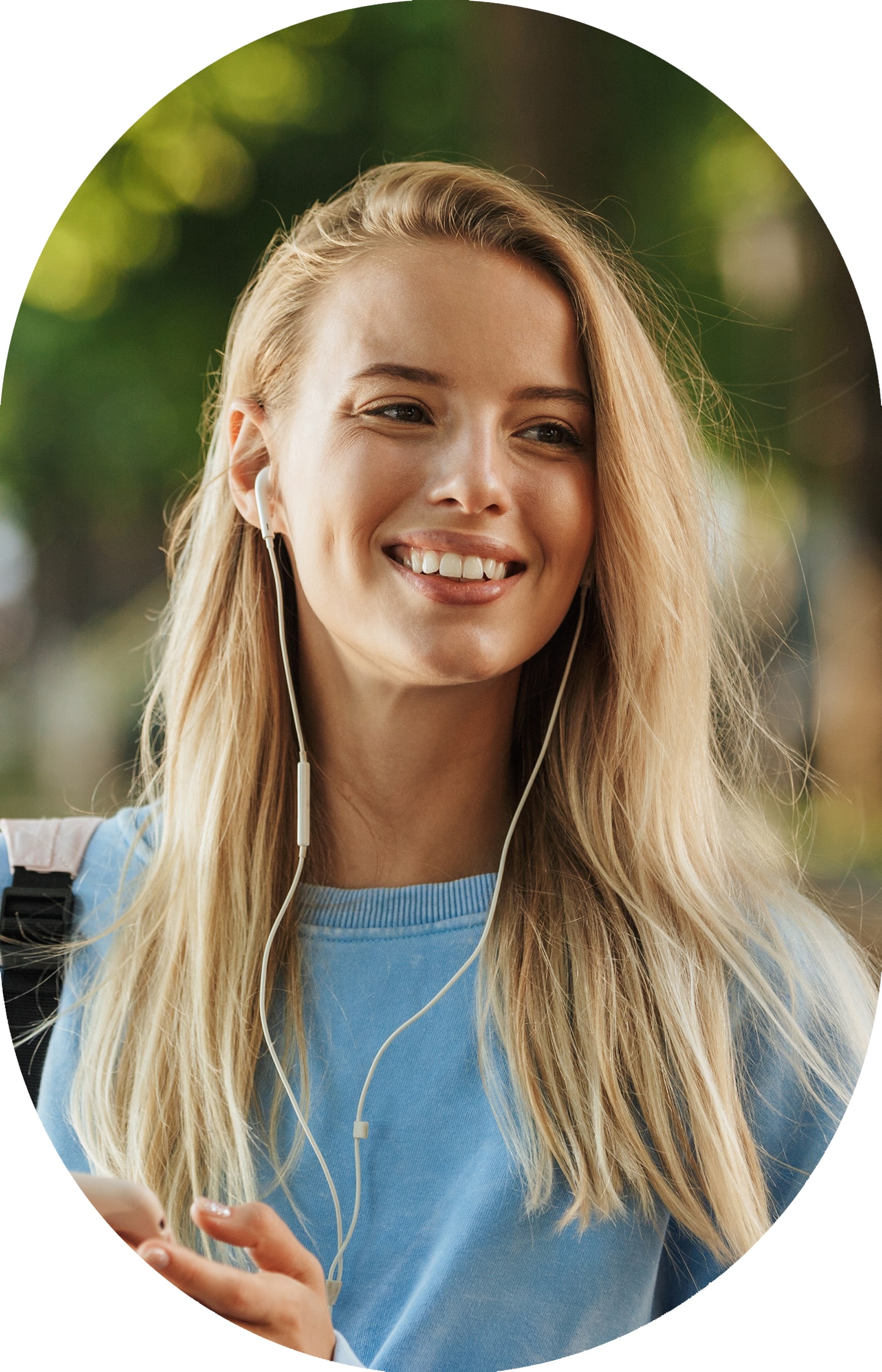 Young smiling woman wearing earbuds standing outside with trees in the background 