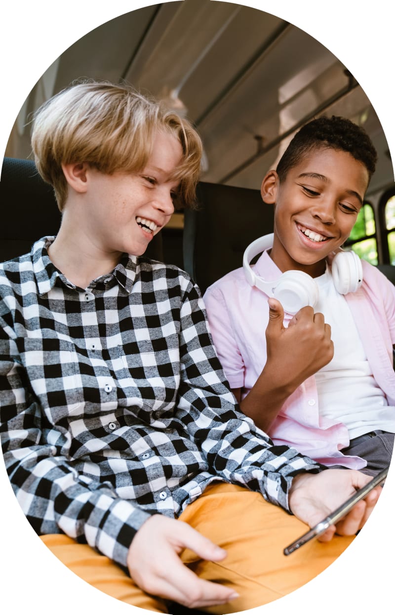 Two boys are sitting together on a bus laughing and smiling.