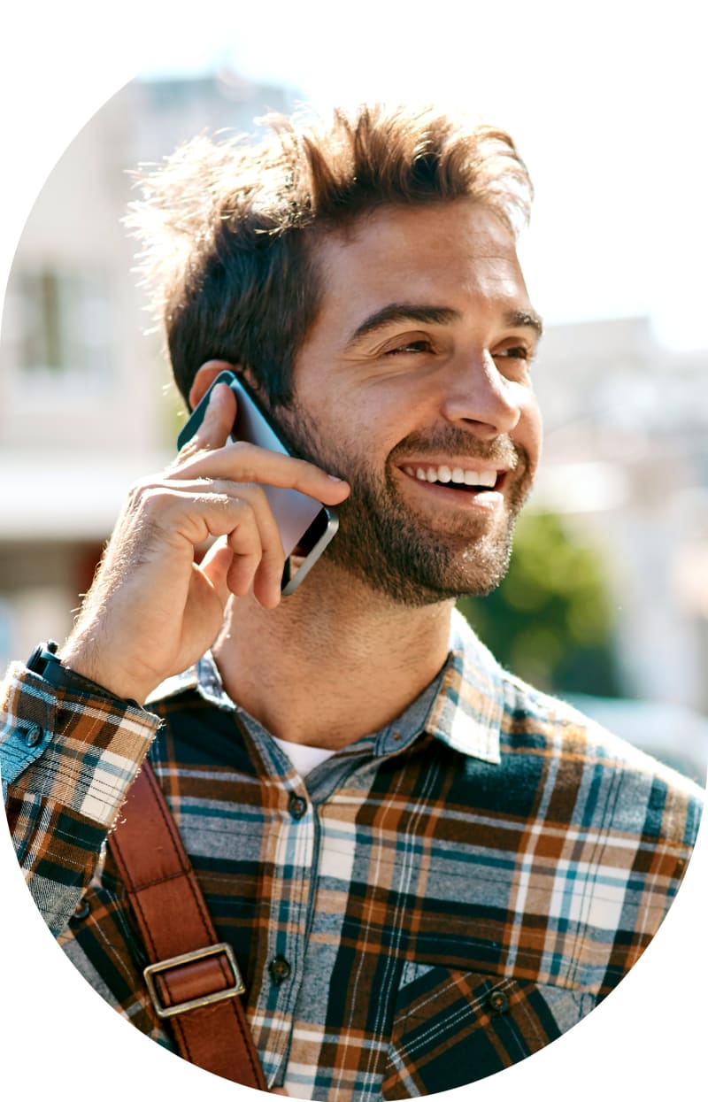 A man wearing a plaid shirt is outside talking on his phone and smiling.
