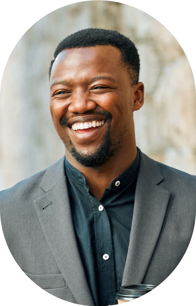 A man in dark grey business attire looks off to the side smiling.