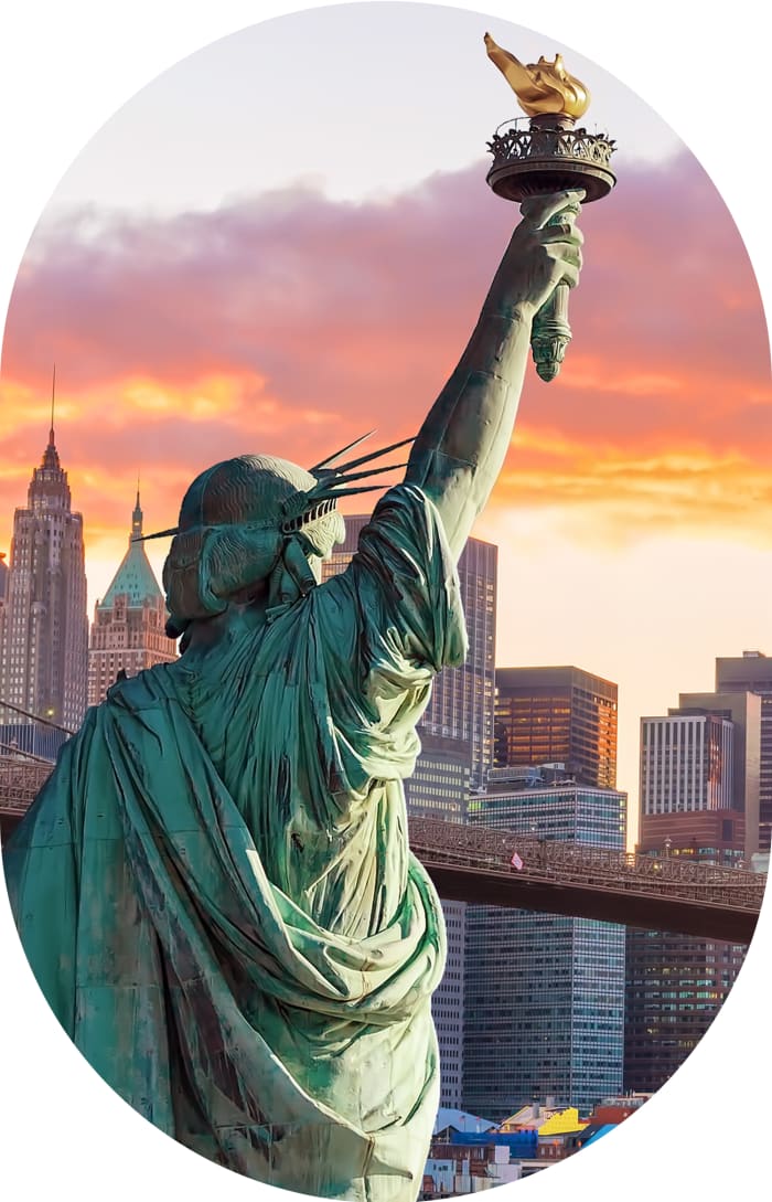 The Statue of Liberty in New York from behind at sunset, with the Manhattan skyline in the background. 