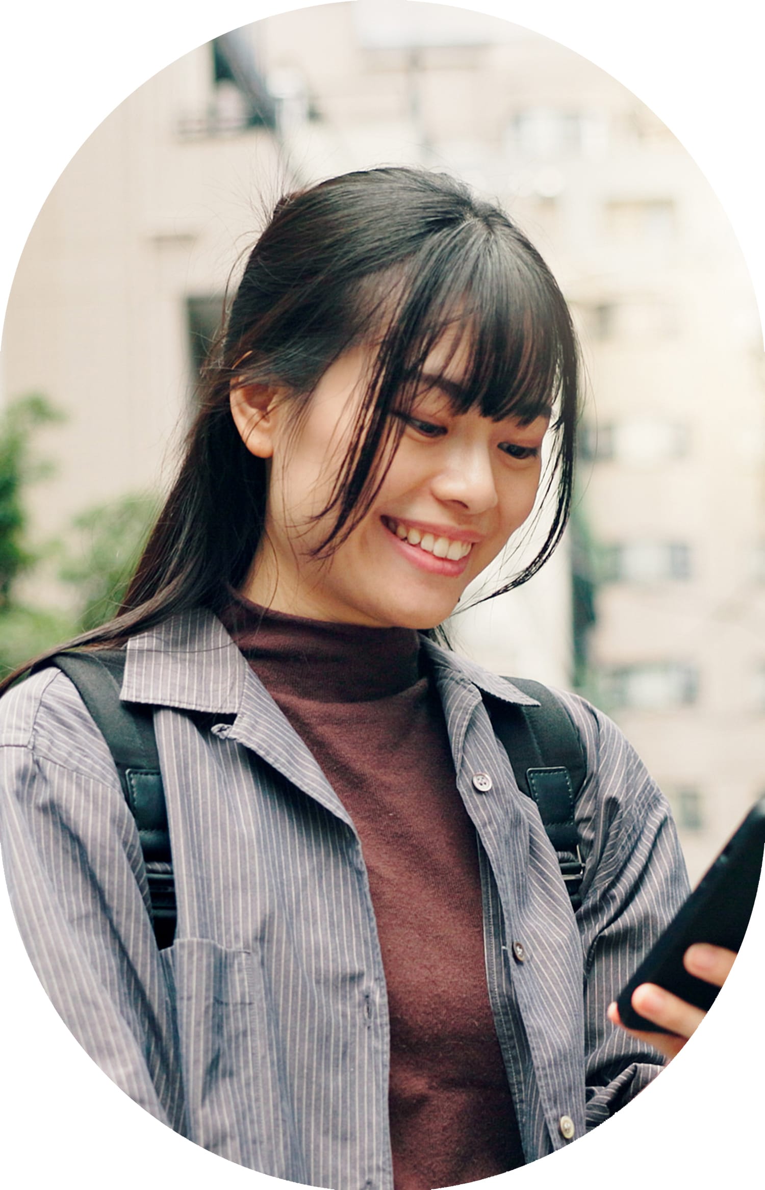 A young woman is smiling down at her phone.