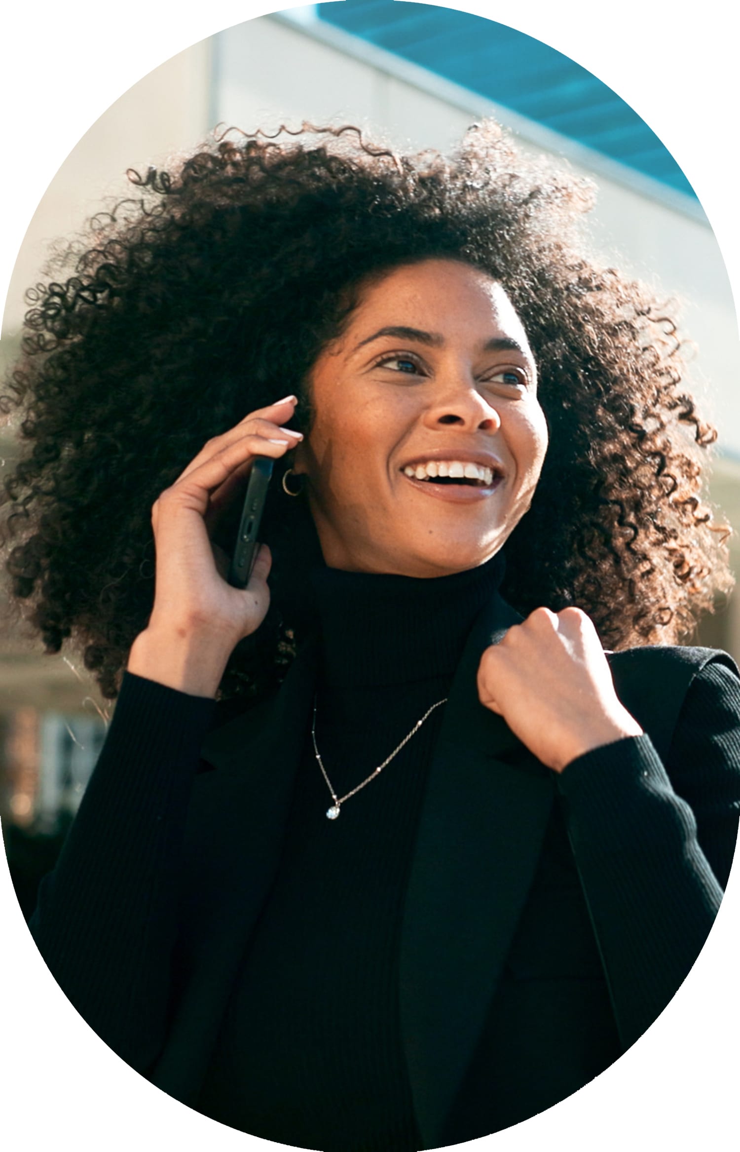 A woman with curly hair smiling and talking on the phone.