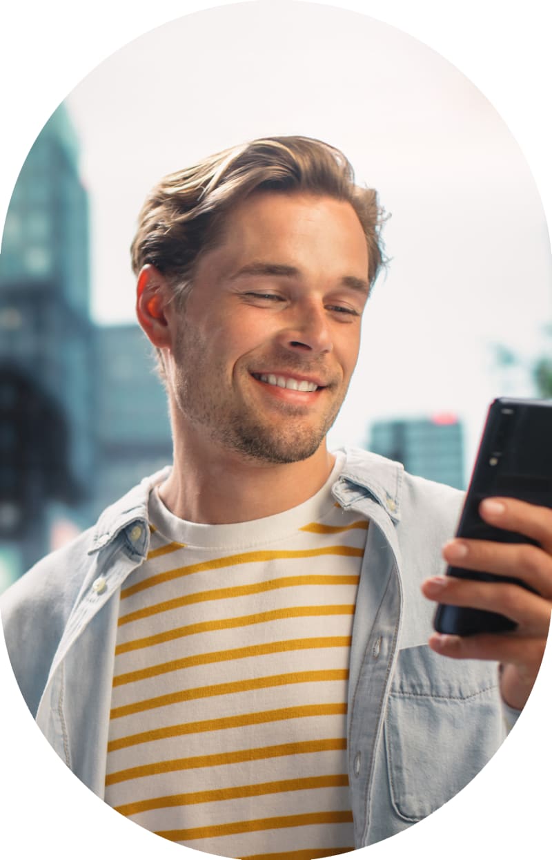 Guy in a blue shirt, smiling while looking at his cell phone.