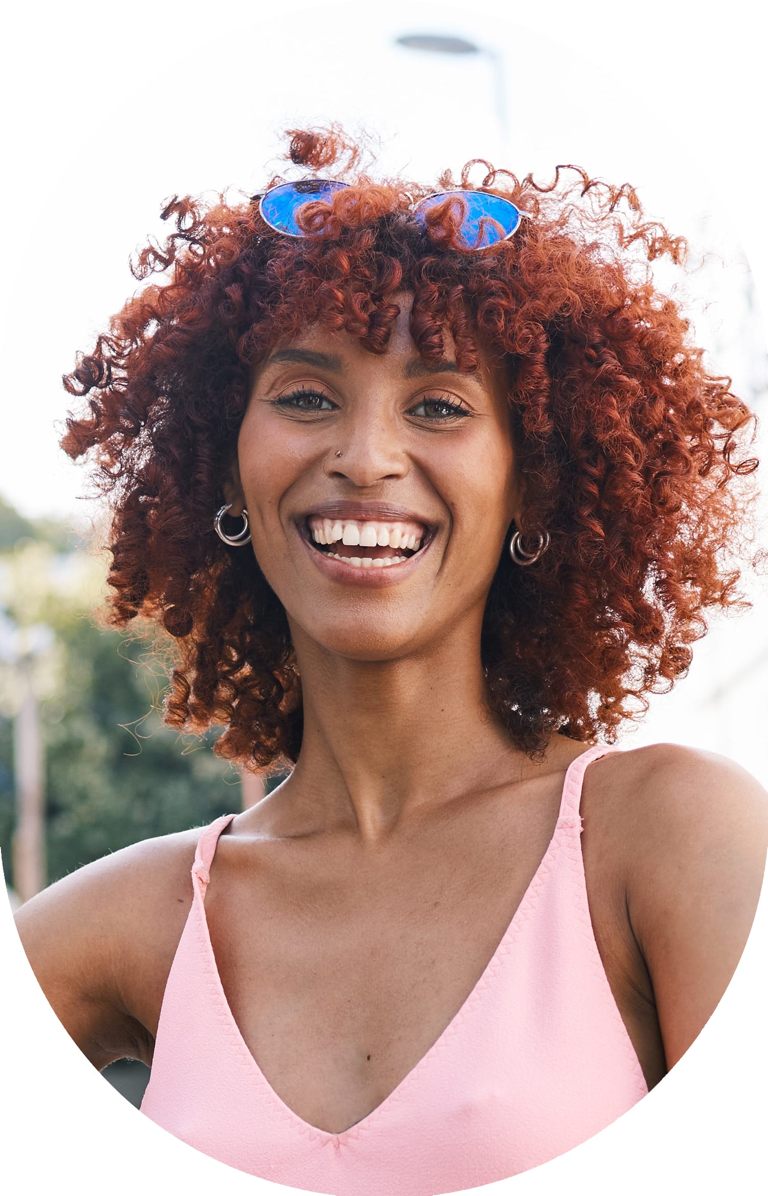 Smiling woman standing outside, with sunglasses resting on the top of her head.