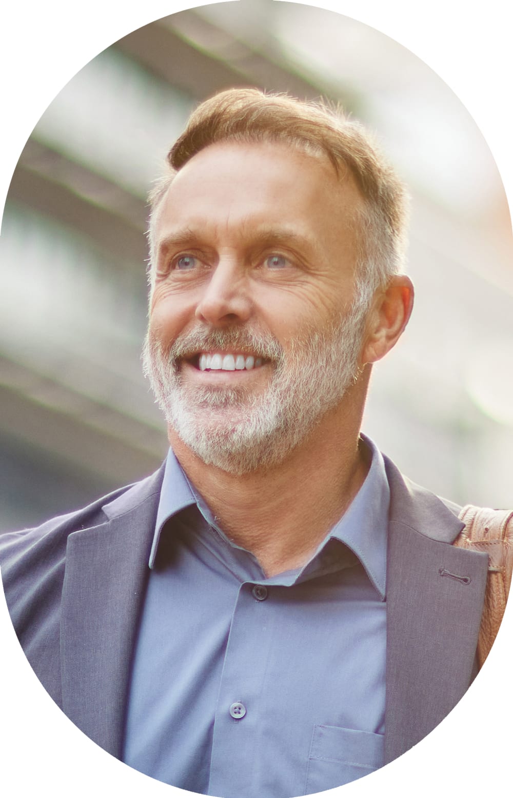 A bunsiness man with a bag strap over his shoulder stands outside smiling.