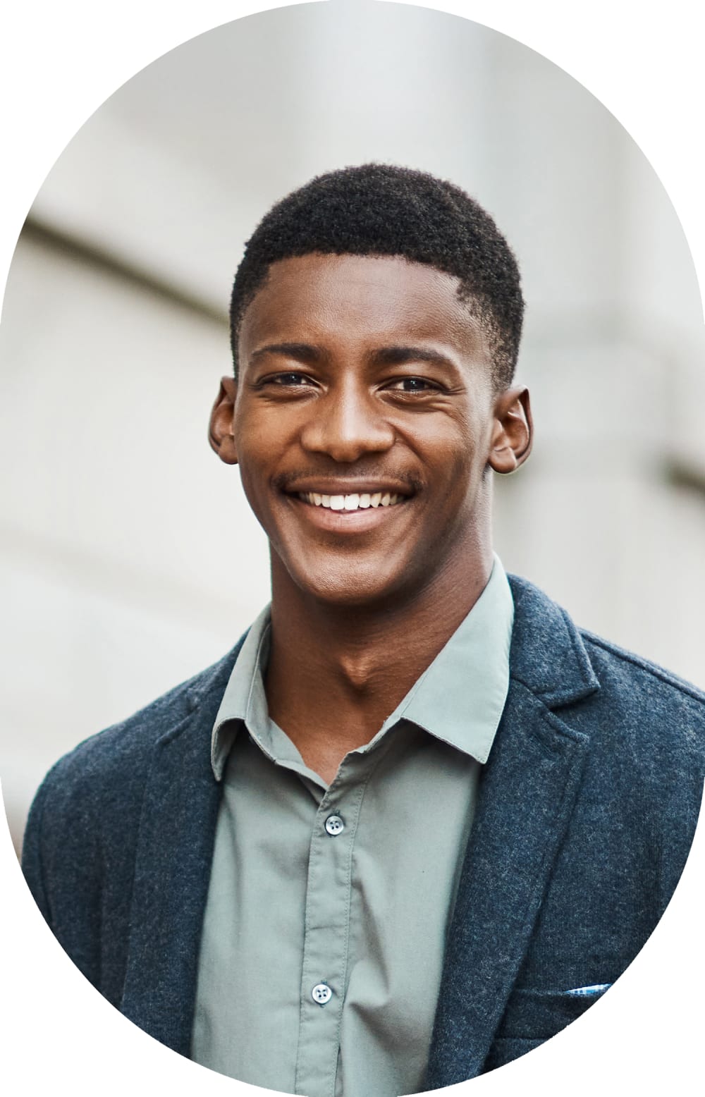 A bunsiness man with a bag strap over his shoulder stands outside smiling.