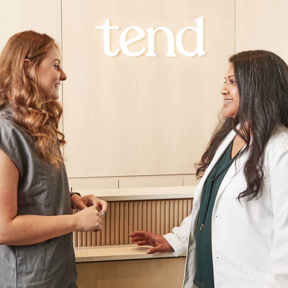 Dentist in a white coat and dental assistant in grey, smiling while talking together.