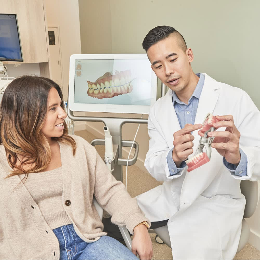 Dentist in a white coat and dental assistant in grey, smiling while talking together.