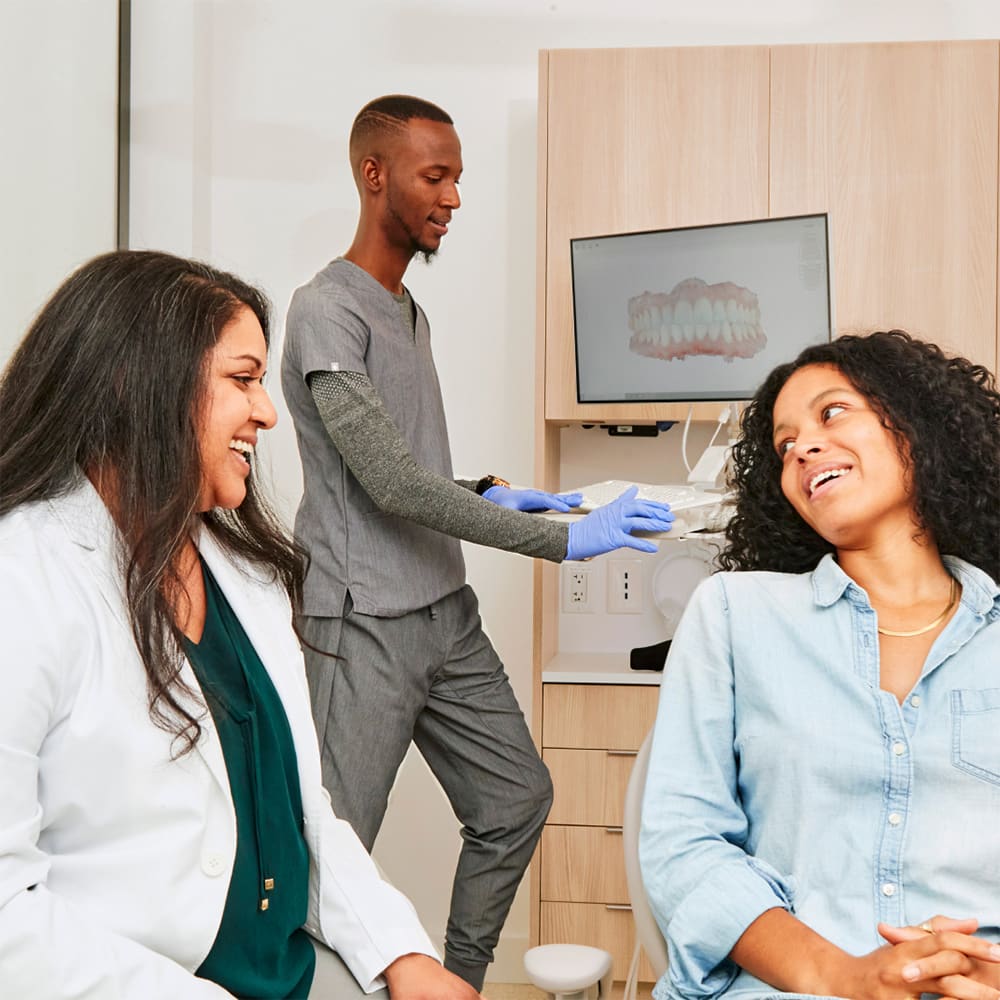 Male dentist pointing to a model of teeth while explaining treatment to a patient seated in the dental chair.