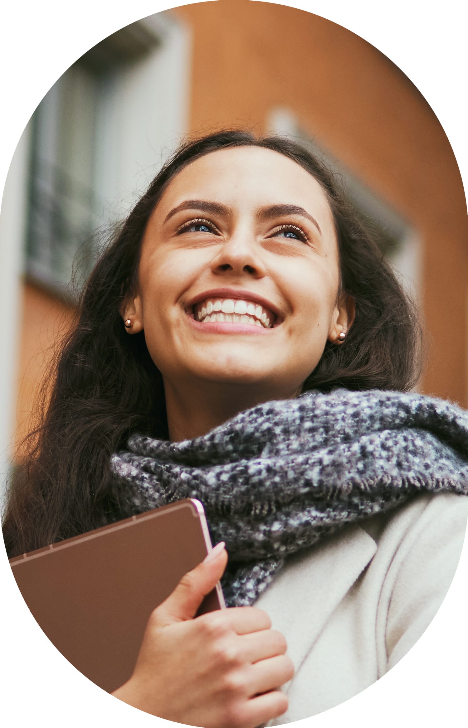 Woman wearing a scarf and holding a laptop, smiling while looking to the right.