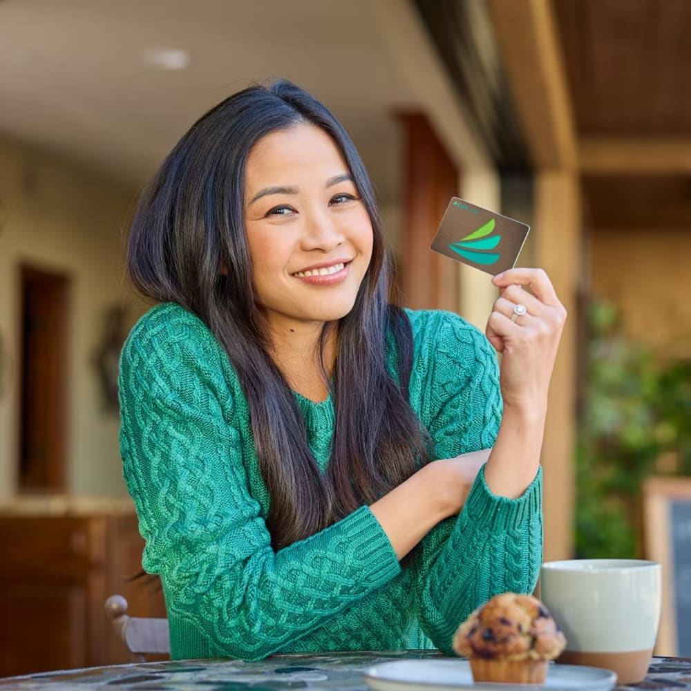 A woman in a green sweater is holding a CareCredit Card.