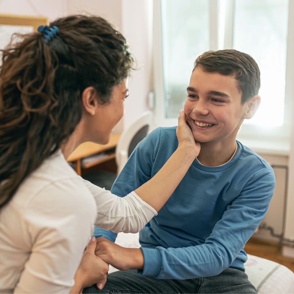 A woman looking at a smiling boy while holding his face in her hand.