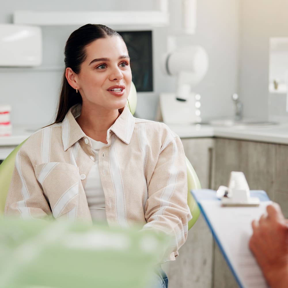 A patient sits in a treatment chair while a dental professional takes notes