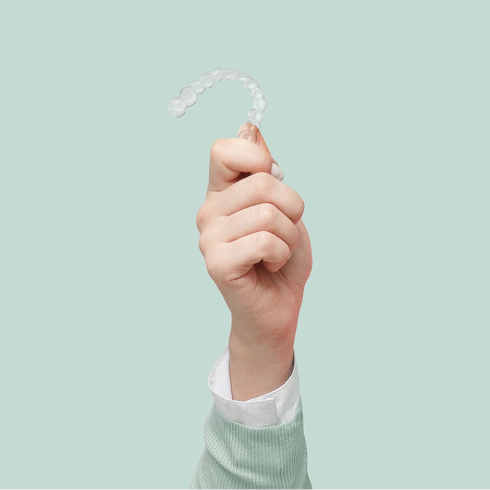 A hand holds up a set of clear aligners