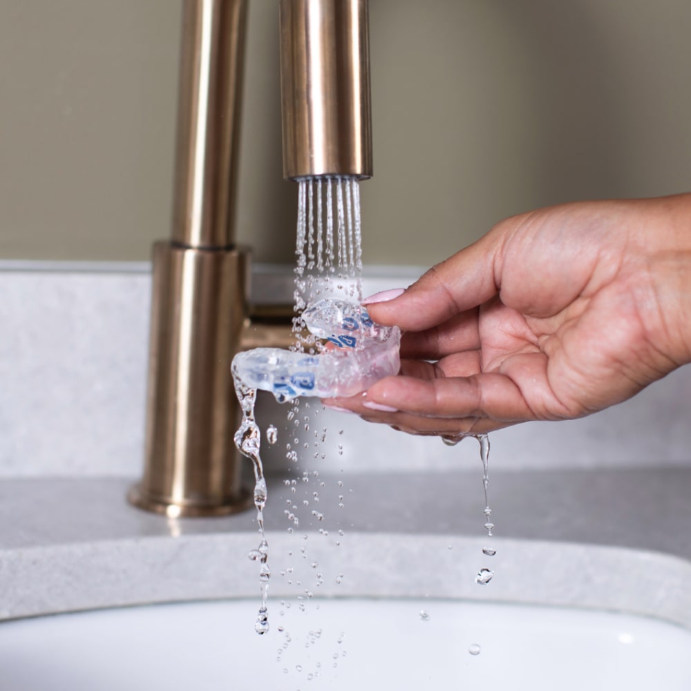 Hands rinse a Perio Protect tray at a sink.