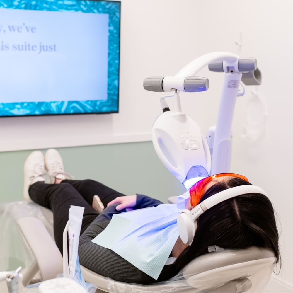 A patient is laying in a dental chair while undergoing a teeth whitening treatment.